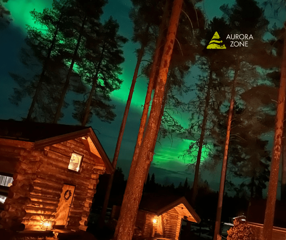 The Northern Lights in Swedish Lapland in the background of trees and a log cabin hut.