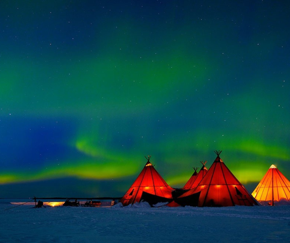 tent like huts lit up by the northern lights in the snow