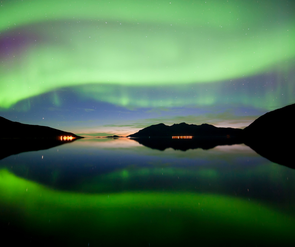 a scene on a lake with mountains lit up by the northern lights